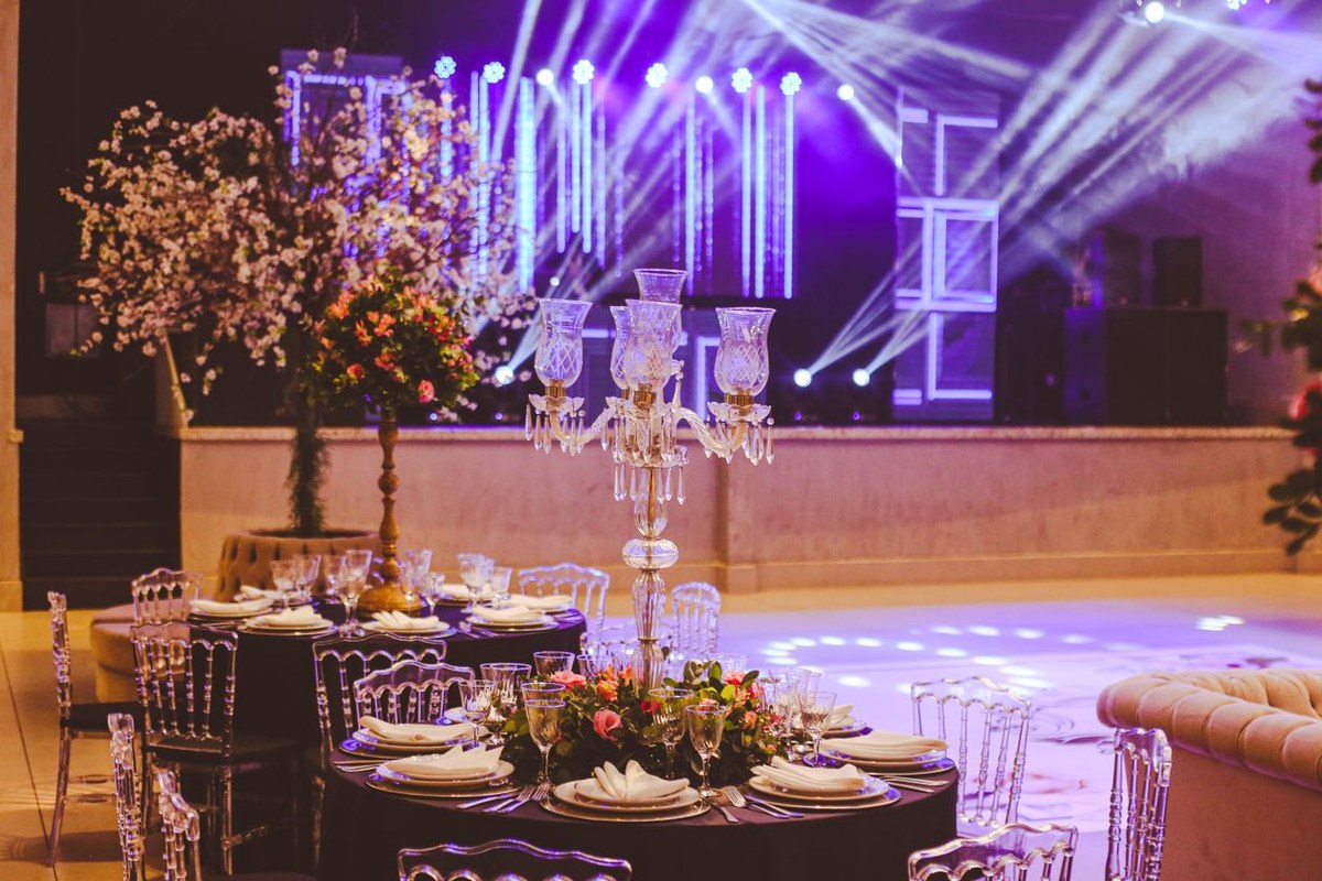 Formal banquet table with crystal candelabra and clear chairs in an event hall lit by purple stage lights